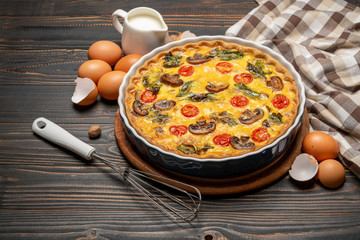 Baked homemade quiche pie in ceramic baking form, eggs and cream