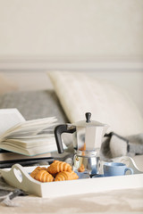 Breakfast in bed. On a white tray there is a coffee maker, coffee blue cup and croissants.