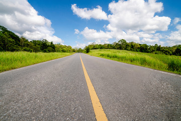 Highway road up hill through green grass field under white clouds on blue sky in summer day. Road...