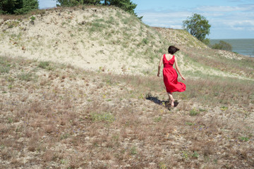 Brunette woman in red dress walks barefoot in the field in summer