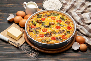 Baked homemade quiche pie in ceramic baking form, eggs and cream