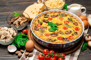 Baked homemade quiche pie in ceramic baking form, eggs and cream