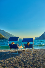 Fototapeta na wymiar People sitting at the beach on the lounge chair and admiring Lake Garda in the summer time,View of the beautiful Lake Garda surrounded by mountains