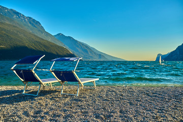 People sitting at the beach on the lounge chair and admiring Lake Garda in the summer time,View of...