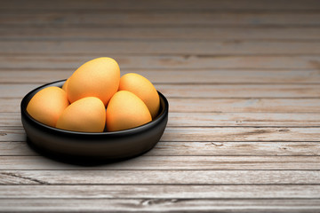 Black shiny bowl with brown eggs standing on the wooden table. Image with copy blank space. 3d illustration.