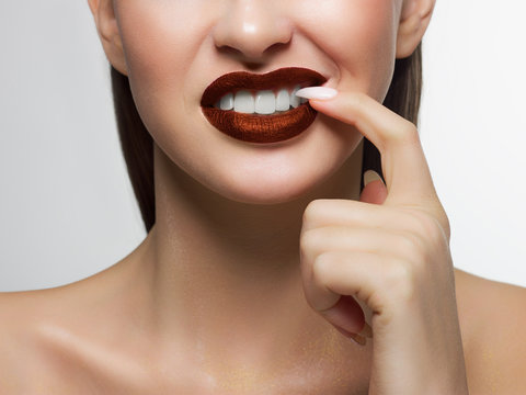 Close-up portrait of the lower half of a woman's face with a malicious grin. He picks a long fingernail in his teeth. Beautiful full lips with a trendy lipstick tint. Dental smile. Teeth whitening