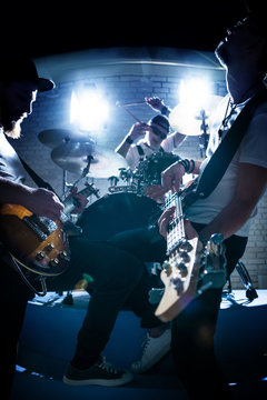 Two guitarists and a drummer play musical instruments