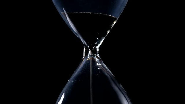 The sand flow in the hourglass with black background and lateral light backlight in centered composition