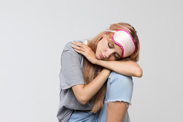 Studio portrait of sleepy young woman in grey t-shirt feels tired after work, sitting on a chair...