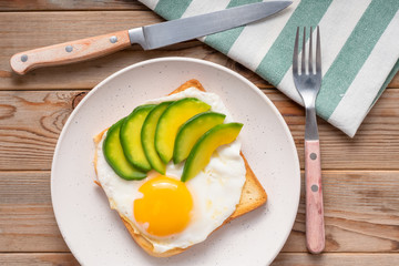 Toast bread with fried eggs, avocado. And cucumber slices on wooden table. Top view.