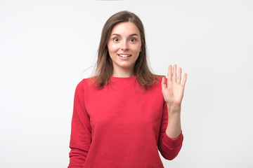 Friendly-looking teenager dressed in red pulover saying hello, waving her hand.