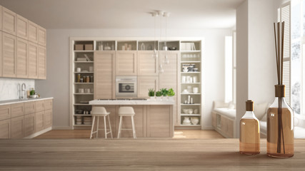 Wooden table top or shelf with aromatic sticks bottles over blurred modern white kitchen with wooden details in contemporary luxury apartment, white architecture interior design