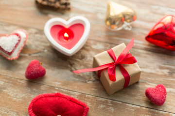 Fototapeta na wymiar christmas, valentines day and holidays concept - gift box with heart shaped decorations and candle burning on wooden background