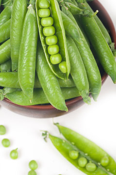 green peas in pods.  in a clay plate on a white background