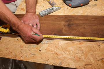 Worker is holding in hands a tape measuring. Power jigsaw for laminate flooring. Maintenance repair works renovation in the flat with scroll saw. Restoration of wooden parquet floor planks.