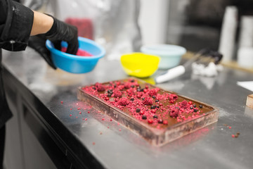 production, cooking and people concept - confectioner making chocolate with berries at confectionery shop kitchen