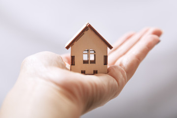 Miniature wooden home design on palm on grey background, concept of business in real estate and real estate