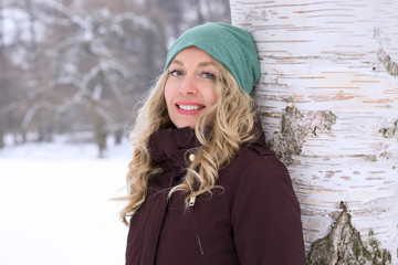smiling woman leaning against birch tree in snow covered winter landscape