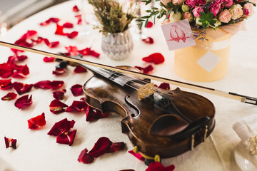 Romantic valentine table setting with wine, dishes, beautiful flowers in box, empty glasses, rose petals, candles, violin © mat_mary