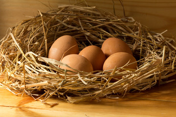 chicken eggs in straw on wooden background