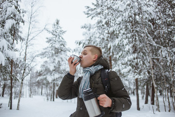 Stylish man with a thermos of hot tea in a snowy conifer forest