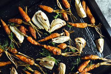 Roasted fennel and baby carrots on tray. Rustic background.
