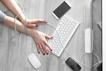 Uzależnienie od nowych technologii.  Kobieta ze związanymi dłońmi kablem pisze na klawiaturze...