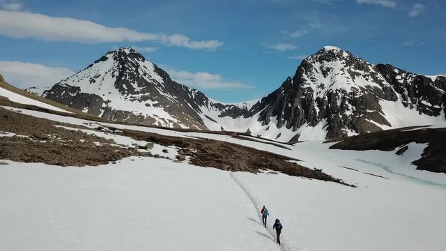 Aerial Drone: Two Men Hiking Towards Patchy Snow-Covered Mountains