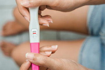 Unhappy young asian woman holding pregnancy test showing a negative result in her bathroom,...