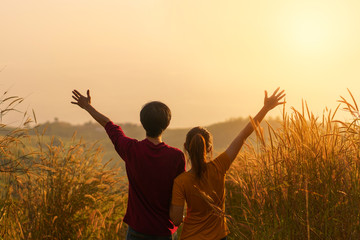 Asian woman and man standing and hand up in meadow and looking far away at sunrise time.