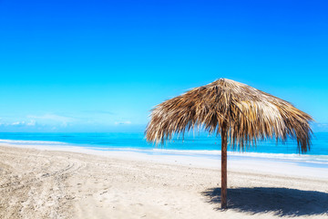 Fototapeta na wymiar Straw umbrella on empty seaside beach in Varadero, Cuba. Relaxation, vacation idyllic background.