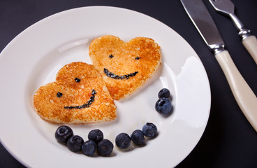 plate of two pancakes in the shape of heart with berries on white table