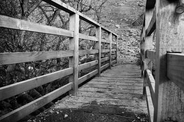 A black and white of a small wooden foot bridge with wooden side barriers