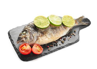 Slate board with grilled dorado fish, lime, tomato and spices on white background