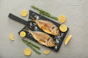 Board with grilled dorado fish and lemon on grey background