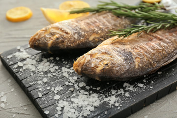 Board with grilled dorado fish and salt on grey background