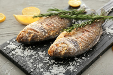 Board with grilled dorado fish and salt on grey background