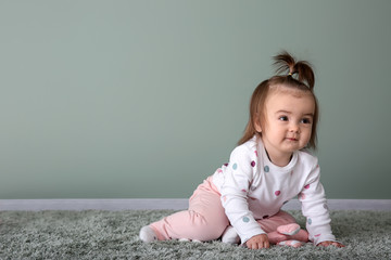 Fototapeta premium Cute baby girl on carpet near color wall