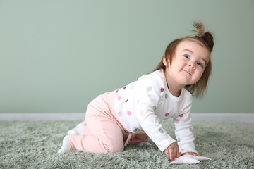 Cute baby girl on carpet near color wall