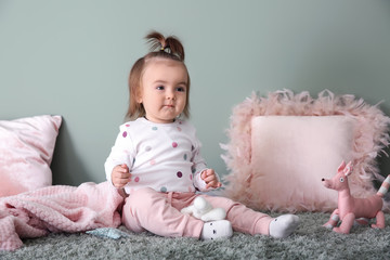 Cute baby girl playing on carpet near color wall