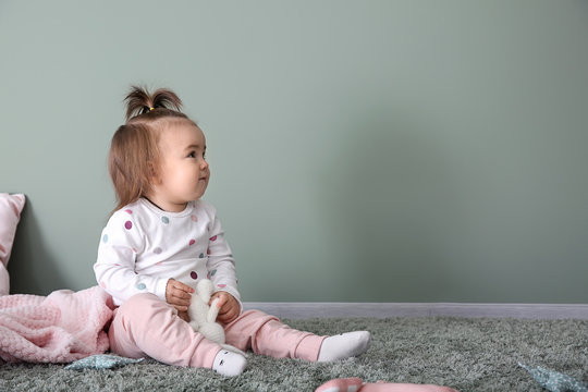 Cute baby girl playing on carpet near color wall