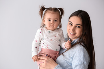 Young mother with her cute little daughter on light background