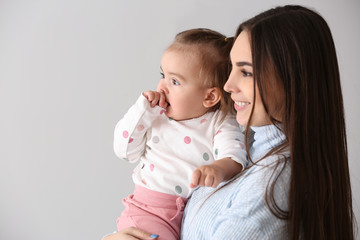 Young mother with her cute little daughter on light background