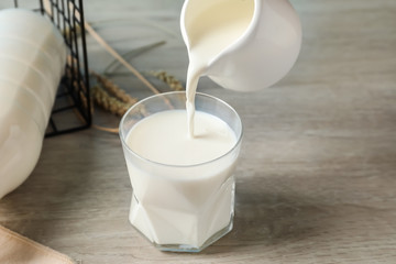Pouring of fresh milk from jug into glass on wooden table