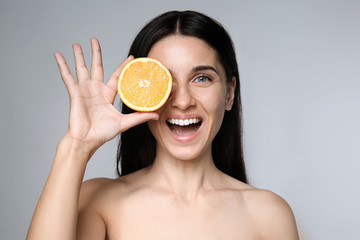 Portrait of beautiful young woman with natural makeup and orange on grey background