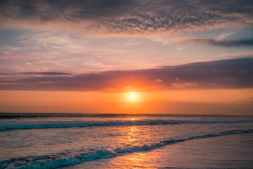 Fototapeta premium Pink and Orange Ocean Waves. Colorful Sunset Waves on Beach. Dramatic Purple Sunset with Twilight Color Sky and Clouds. Surfing Silhouette Landscape Background of Sunrise Ocean for Surf and Surfers. 