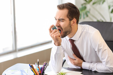 Young man with inhaler having asthma attack in office
