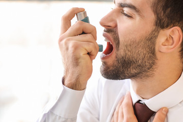 Young man with inhaler having asthma attack in office
