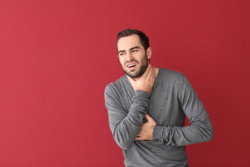 Young man having asthma attack on color background