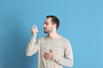 Young man with inhaler on color background